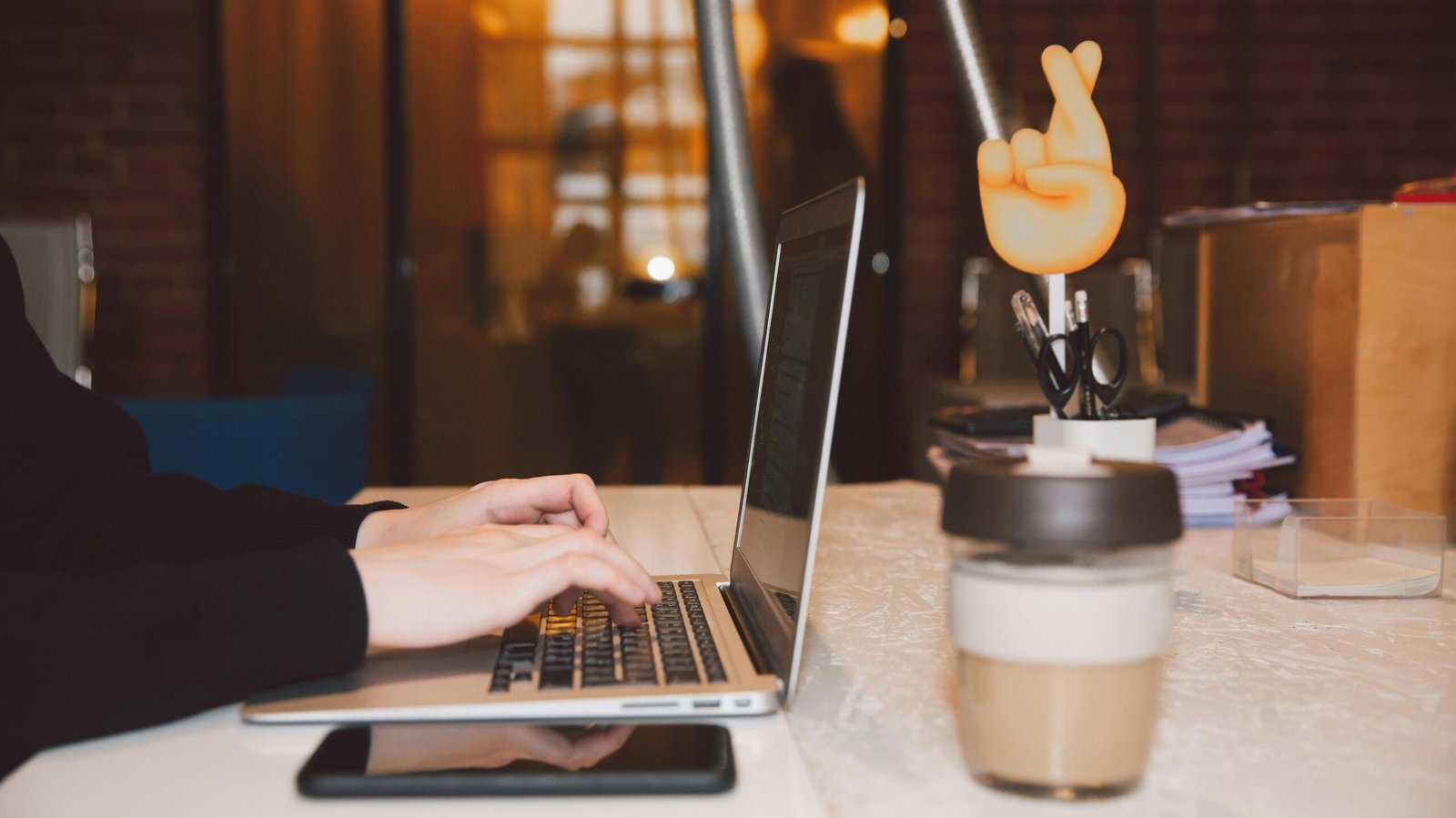 Close-up of hands typing on a laptop in a modern office setting with coffee and creative decor.