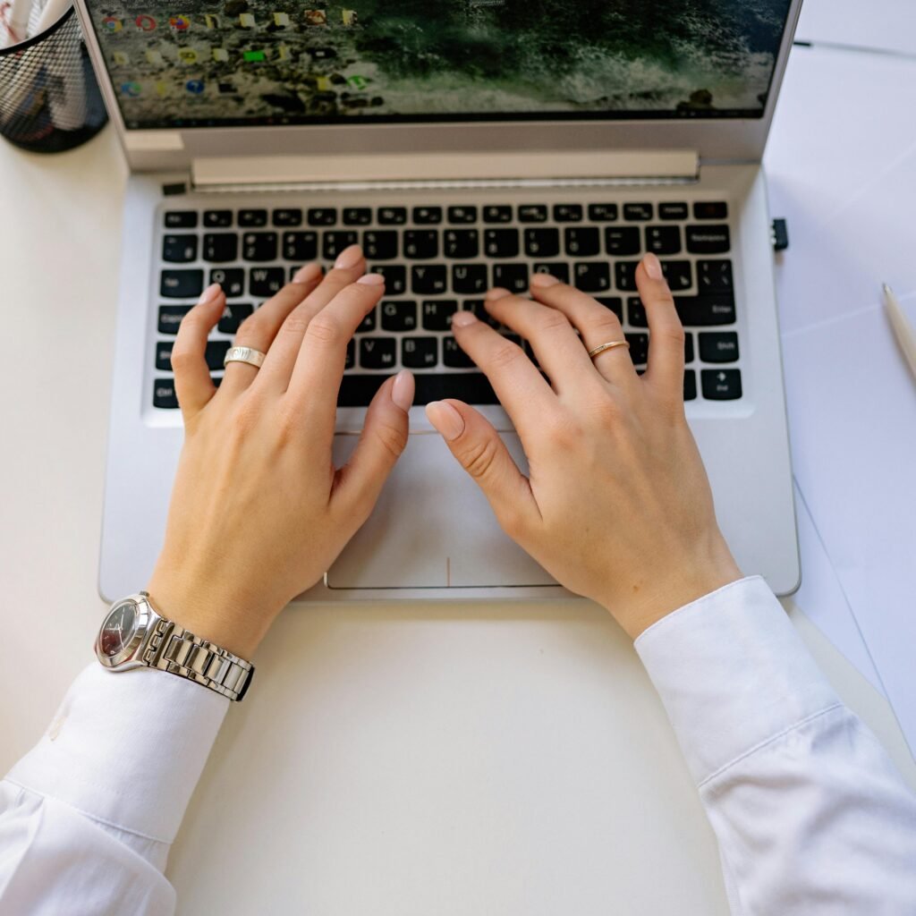 Hands typing on a sleek laptop keyboard in a bright, modern workspace. Ideal for business concepts.